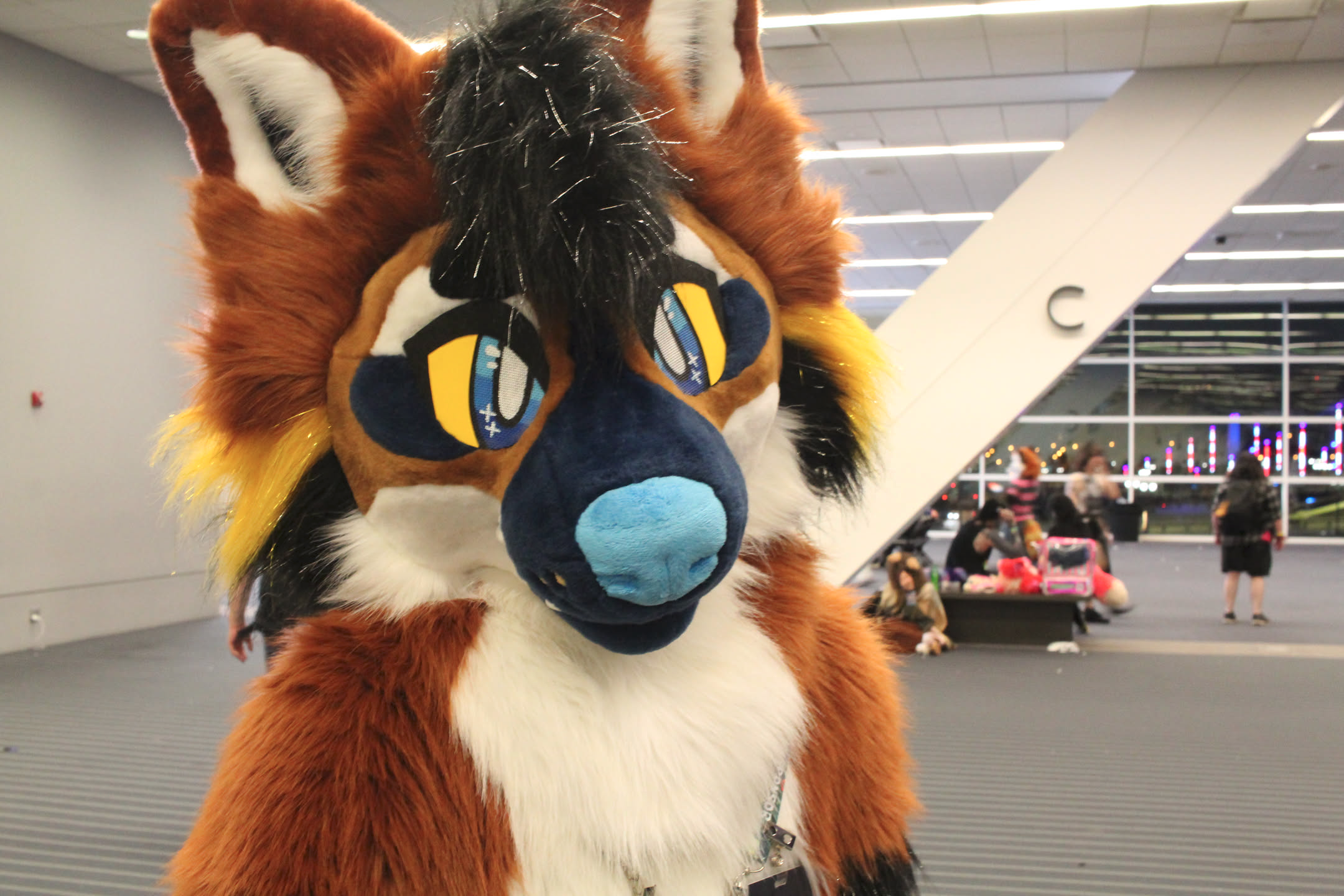 maned wolf fursuiter milling about a convention center with some blurry people in the background